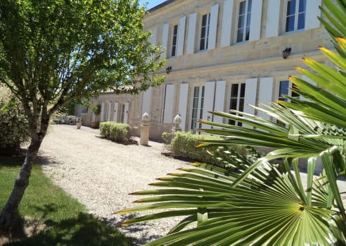 Elegant pati de mansió de pedra amb camí de grava, plantes de palma i paisatgisme verd a Le Manoir Lacustre B&B a Queyrac