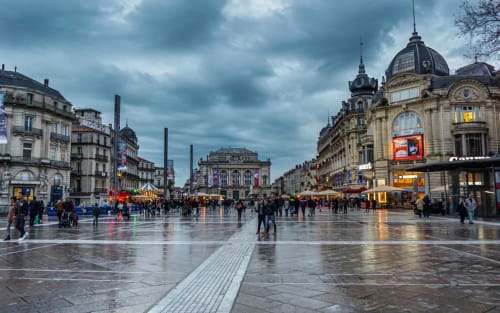 Soirée pluvieuse à la place historique de Montpellier avec bâtiments Belle Époque illuminés et foules