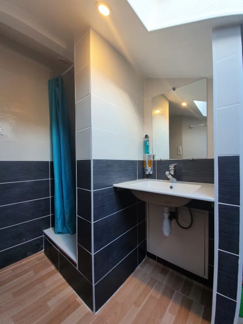 Salle de bains moderne à la Chambre B de NancyRoom à Vandoeuvre-les-Nancy, avec carrelage noir, lavabo blanc et rideau de douche turquoise