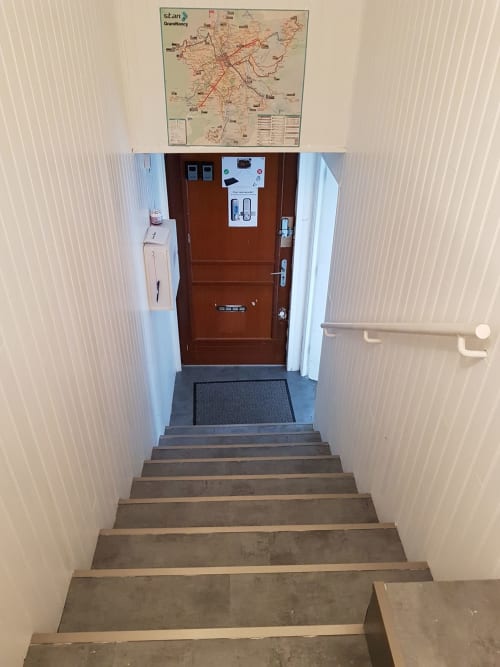 Entrée escalier NancyRoom B&B avec porte marron, carte murale et paillasson à Vandoeuvre-les-Nancy