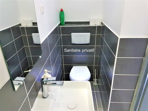 Salle de bain privée moderne aux murs carrelés sombres, toilettes blanches, lavabo avec robinetterie chromée et articles de toilette à NancyRoom B&B