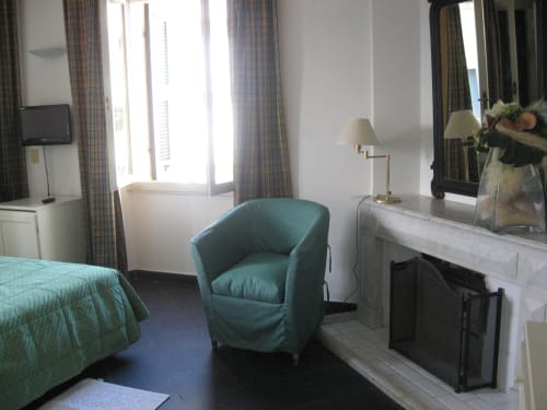 Klassisches Zimmer des Hotel Beau Rivage in Alassio mit türkisem Sessel, Kamin, Schreibtisch und Stadtblick