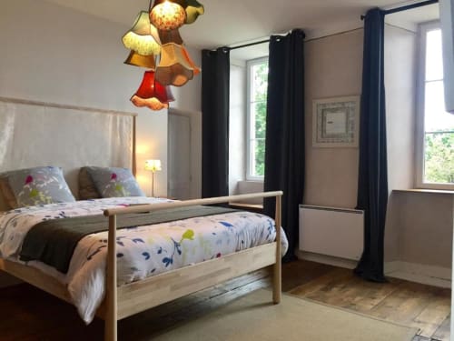 Chambre double lumineuse à L'Ermitage B&B avec lit en bois, literie colorée, rideaux noirs et lampes suspendues