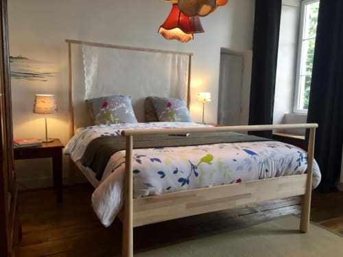 Chambre double lumineuse à L'Ermitage B&B avec lit en bois, literie fleurie, vue sur le jardin et éclairage chaleureux