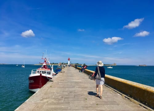 Jetée de Saint-Vaast-la-Hougue avec bateau de pêche rouge et touristes, mer et ciel bleus