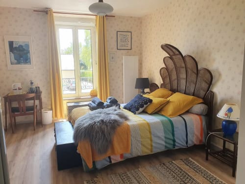 Chambre lumineuse avec tête de lit en rotin, literie jaune et balcon avec vue sur Jugon-les-Lacs aux Forges Du Lou