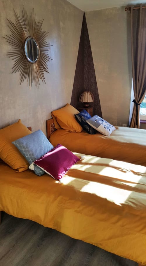 Lits jumeaux avec literie orange éclatante et coussins colorés aux Forges Du Lou B&B à Jugon-les-Lacs, chambre baignée de lumière naturelle