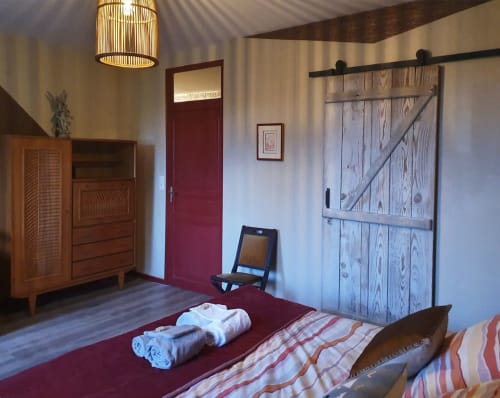 Spacieuse chambre aux Forges Du Lou avec mur d'accent rouge, porte grange, commode en bois et literie rayée à Jugon-les-Lacs.