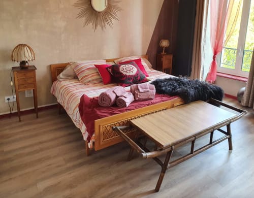 Chambre La vallée de Dana aux Forges Du Lou avec lit en bois, literie rayée, coussins rouges, table de nuit et portes-fenêtres