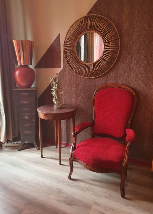 Élégante chambre aux Forges Du Lou avec fauteuil rouge, mobilier en bois et miroir rond à Jugon-les-Lacs