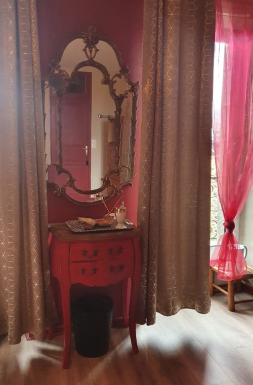 Élégante coiffeuse rouge avec miroir orné et rideaux marron dans la chambre La vallée de Dana aux Forges Du Lou, Jugon-les-Lacs