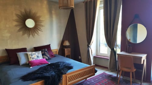 Chambre élégante aux Forges Du Lou avec lit bleu, mur d'accent violet, miroir soleil et vue sur balcon à Jugon-les-Lacs