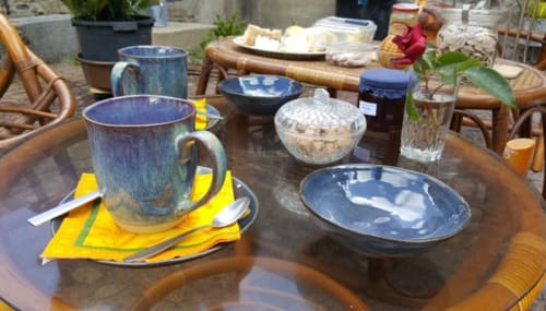 Table de petit-déjeuner en plein air à Les Forges Du Lou avec vaisselle céramique bleue, serviettes jaunes et viennoiseries fraîches