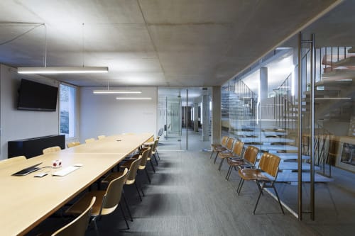 Modern conference room at Mas De Lafeuillade in Montpellier with long table, wooden chairs, glass partitions, and skylight