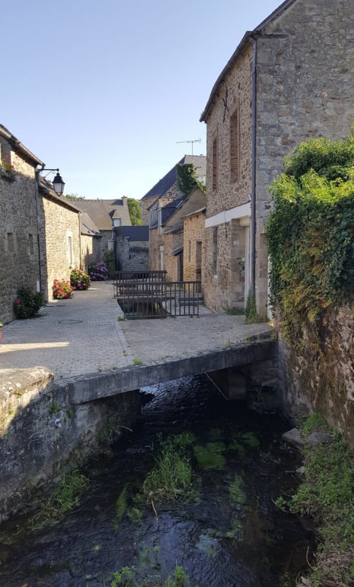 Pittoresque rue de village en pierre aux Forges du Lou avec ruisseau et bâtiments traditionnels à Jugon-les-Lacs