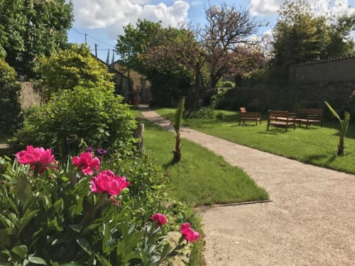 Le jardin de l'Ermitage avec pivoines roses, allée de gravier et bancs en bois à Saint-Vaast-la-Hougue