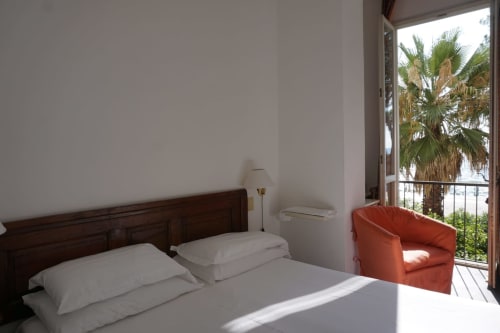 Schlafzimmer des Hotel Beau Rivage in Alassio mit Meerblick, Palmen, Holzbett und orangem Sessel