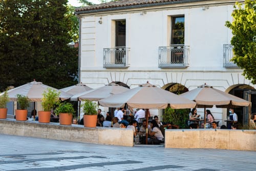 Outdoor terrace at Mas De Lafeuillade in Montpellier with umbrellas, guests dining, and white historic building