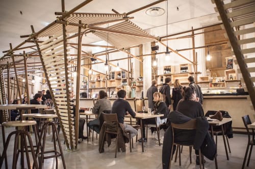 Modern café interior at Mas De Lafeuillade in Montpellier with wooden pergolas, shelving, and guests dining