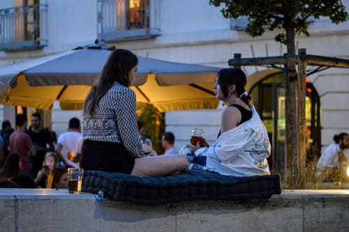 Two women enjoying drinks at twilight in Montpellier, France, near a yellow awning and outdoor seating area at Mas De