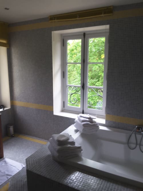 Salle de bains luxueuse au Château de Ré avec baignoire, portes-fenêtres donnant sur le jardin, murs carrelés gris aux finitions dorées