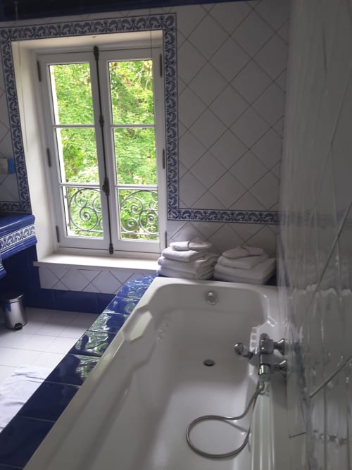 Salle de bains élégante du Château de Ré avec baignoire îlot, portes sur jardin, touches de carrelage bleu et serviettes pliées