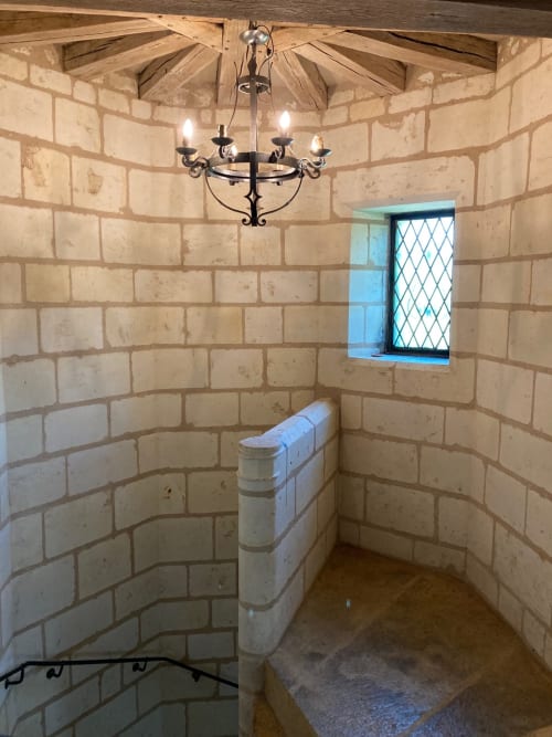 Chambre de tour médiévale au Château de Ré avec murs en briques cintrées, lustre, petite fenêtre treillissée et banc blanc