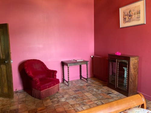Chambre Cardinale du Château de Ré avec murs rose vif, fauteuil en velours bordeaux et mobilier ancien au Petit