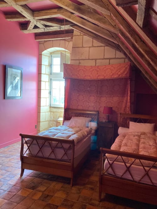 Chambre Cardinale au Château de Ré avec lits jumeaux, poutres apparentes, murs rose et vue sur le jardin