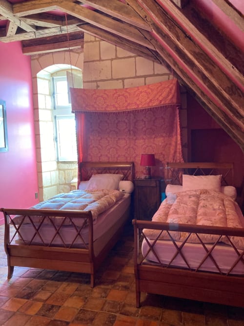 Chambre Cardinale au Château de Ré avec deux lits en bois, dais en damas rouge et poutres apparentes au Petit Pressigny