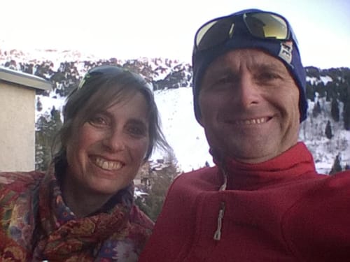 Smiling couple at L'étape Du Fanfoué with snow-covered Chamrousse mountains in background