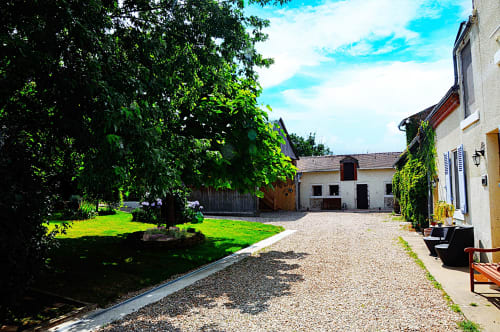 Aux Prés Du Berry courtyard with gravel path, ivy-covered buildings, green lawn and trees in Chavin, France