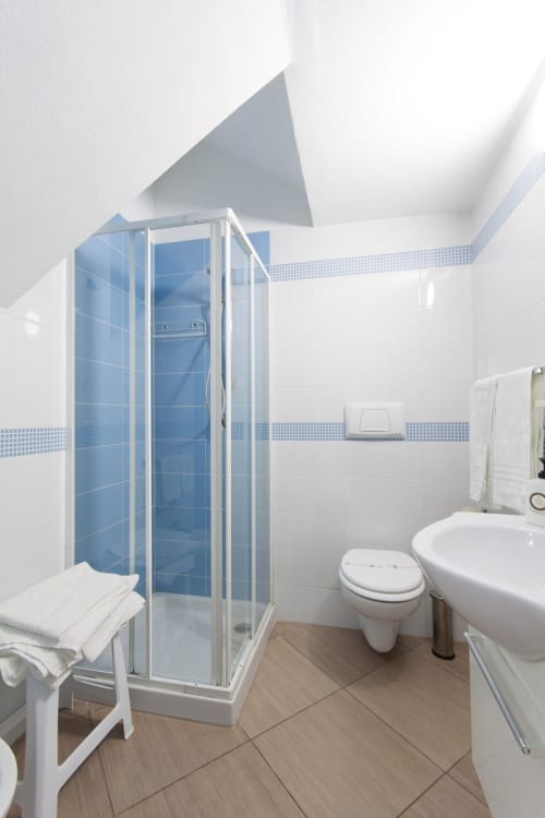 Modern bathroom with blue tile shower enclosure, white sink, toilet, and wooden flooring in Studio Blu apartment at Casa