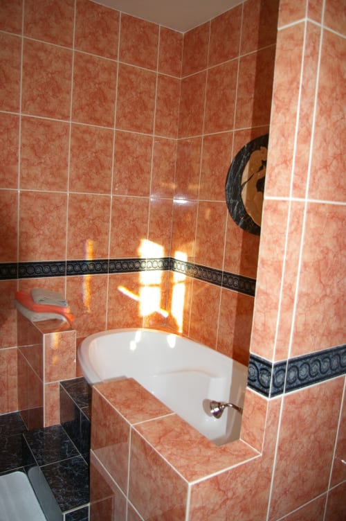 Salle de bains Agnès Sorel au Château de Ré avec murs en carreaux de terre cuite, bordure noire décorative, lavabo blanc et miroir