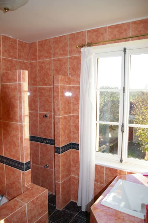 Salle de bains moderne avec douche en carrelage terracotta, baignoire et vue sur le jardin au Château de Ré au Petit Pressigny