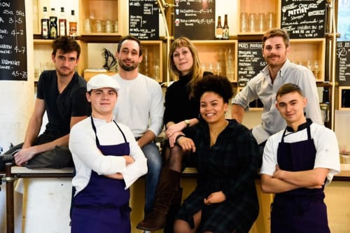 Diverse hospitality team at Mas De Lafeuillade in Montpellier posing in front of shelving with bottles and menu boards