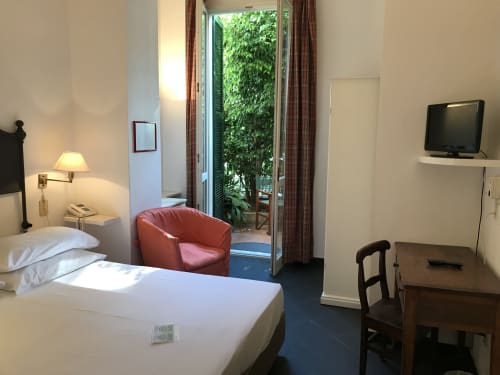 Chambre d'hôtel lumineuse au Beau Rivage Alassio avec lit, fauteuil rouge, portes-fenêtres sur jardin, TV et bureau