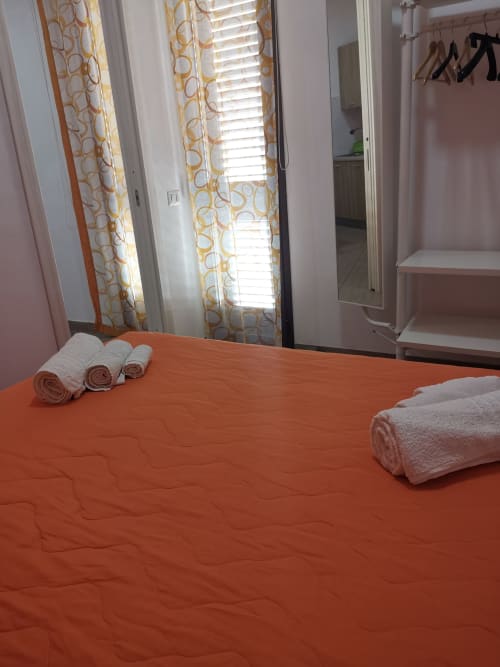 Bright bedroom at Casa Vacanze Del Golfo with orange bedspread, rolled towels, and patterned curtains framing windows in