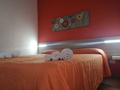 Modern bedroom in Casa Vacanze Del Golfo with orange bedding, rolled towels, red accent wall, and contemporary decor in