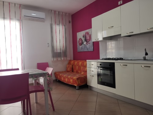 Cucina-soggiorno moderno a Casa Vacanze Del Golfo a Castellammare del Golfo con parete d'accento fucsia e armadiatura bianca