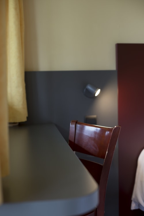 Chambre d'hôtel moderne au Mape Hotel avec chaise en bois, mur d'accent foncé et éclairage tamisé