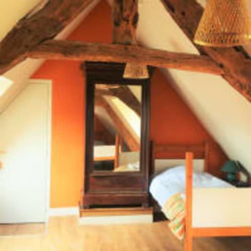 Chambre chaleureuse de la Vieille Foulonnière à Pontorson avec poutres apparentes, murs orangés et mobilier bois rustique