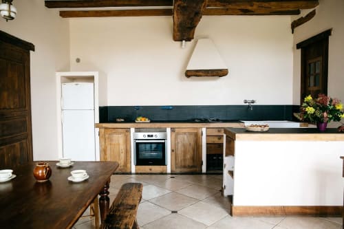 Cuisine rustique de La Vieille Foulonnière avec poutres en bois, plans de travail sombres, salle à manger et vue sur le jardin