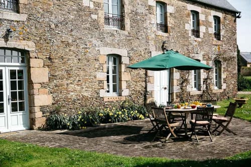 Terrasse en pierre avec parasol vert et mobilier de jardin à La Vieille Foulonnière, Pontorson