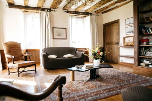Grand séjour de la maison d'hôtes La Vieille Foulonnière à Pontorson avec poutres apparentes, canapé sombre, chaise bois et jardin