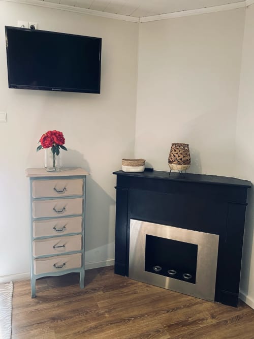 Gemütliche Sitzecke in La Maison de la Colline mit Wandfernseher, schwarzem Kamin und hellblauem Sideboard mit roten Rosen