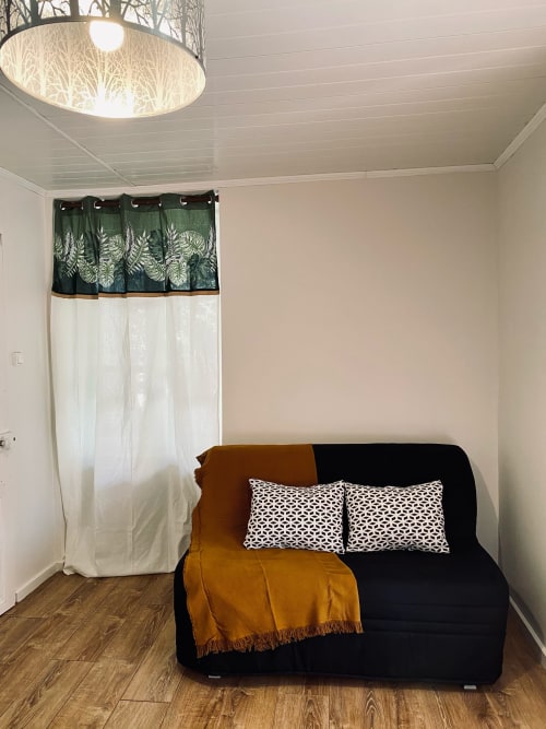 Gemütliche Sitzecke im La Maison de la Colline B&B mit schwarzem Sofa, gemusterten Kissen und Fenster mit Gartenblick