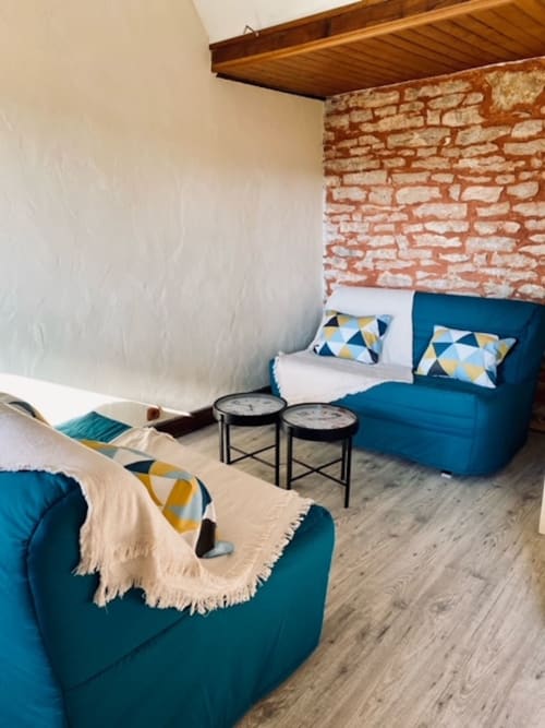 Moderner Wohnbereich im La Maison de la Colline mit petrolblauen Sofas, geometrischen Kissen, Backsteinakzentwand und Holzdecke