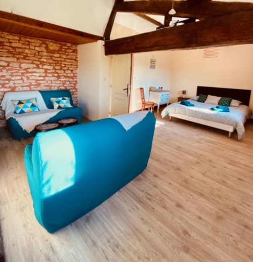 Geräumiges Schlafzimmer in La Maison de la Colline mit blauem Sitzbereich, Deckenbalken, Backsteinwand und Gartenblick