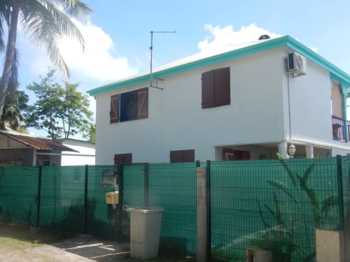 Caribgites BnB à Sainte-Anne, Guadeloupe : maison deux étages blanc et turquoise avec portail vert et palmiers
